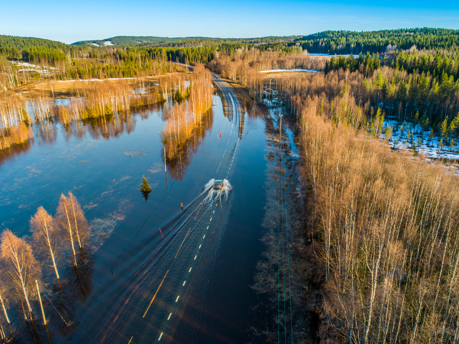 Bild ovanifrån av en bil som kör genom vatten på en översvämmad väg.